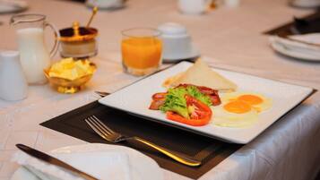 Un desayuno con un plato de huevos, tocino y verduras, un vaso de zumo de naranja y una jarra de leche sobre una mesa.