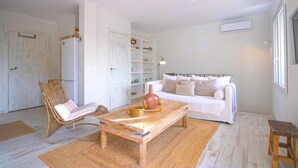 A living room with a white sofa, a wicker chair, a wooden coffee table, and a bookshelf.