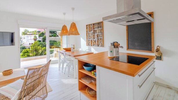 A modern kitchen with a wooden countertop, white cabinetry, and a large window overlooking a garden.
