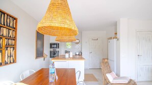 A spacious kitchen with a central island, a dining area with a wooden table, and a wicker chair.