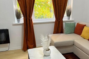 A living room with a beige sofa, a white coffee table, and a potted plant. - Central Birmingham Cozy Apartment (Birmingham)