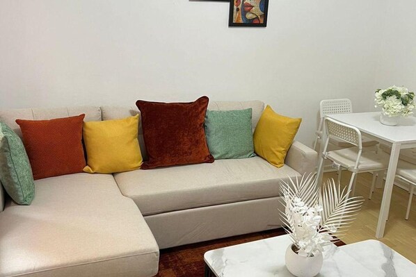 Un salon moderne avec un canapé blanc, des coussins colorés, une table basse blanche et une chaise blanche.