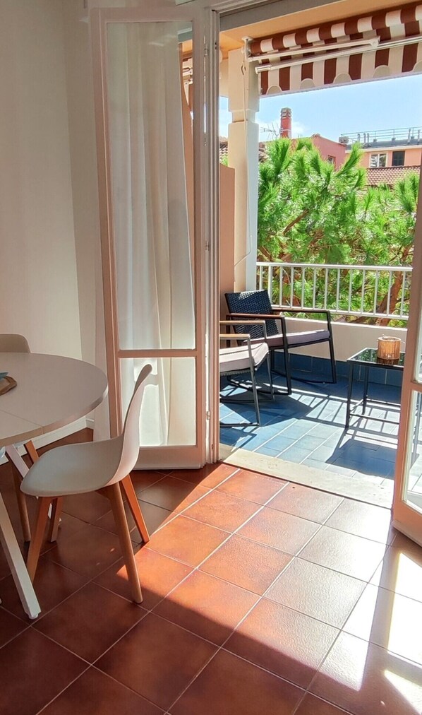 A balcony with a table and chairs, a view of the surrounding buildings, and a tiled floor.