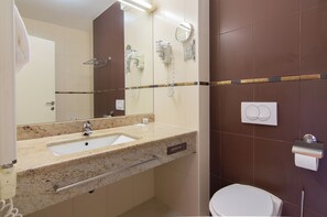 Une salle de bain équipée d’un lavabo, d’un miroir, d’un sèche-cheveux et de toilettes.