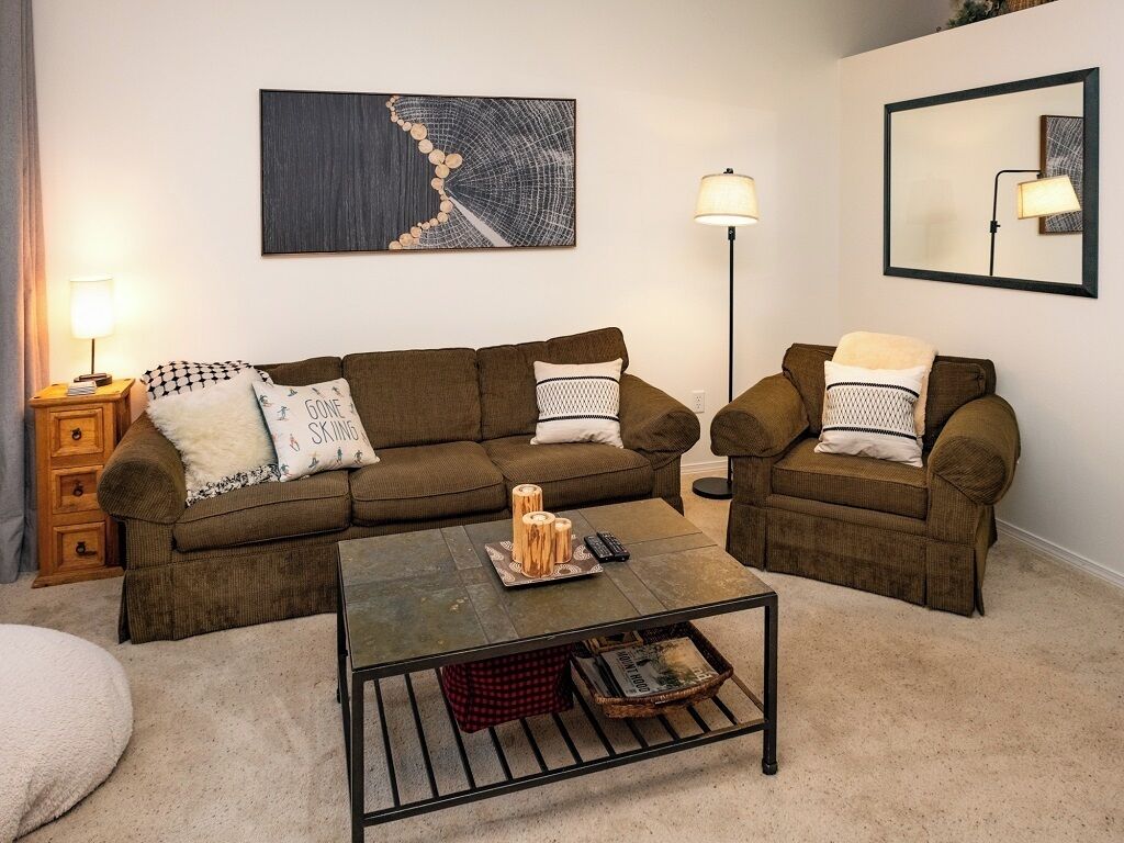 A living room with a brown sofa set, a coffee table, a lamp, and a painting on the wall.