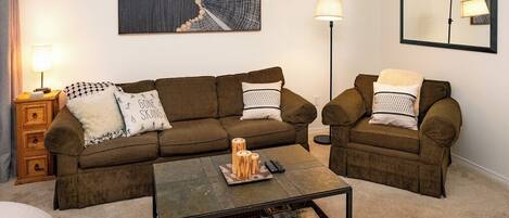 A living room with a brown sofa set, a coffee table, a lamp, and a painting on the wall.