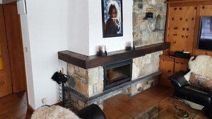 A living room with a stone fireplace, wooden beams, and a black leather sofa.
