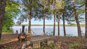 A lakeside campsite with a fire pit, a bench, and a wooden structure. - Charming 2-bedroom lakefront cottage in Central Maine with WiFi (Windsor)
