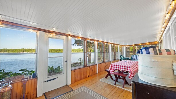A covered outdoor area with a wooden deck, a table with a checkered tablecloth, and a large cake on a stand. - Charming 2-bedroom lakefront cottage in Central Maine with WiFi (Windsor)