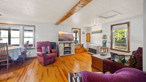 A spacious living room with hardwood floors, a fireplace, a television, and a dining area with a table and chairs. - Charming 2-bedroom lakefront cottage in Central Maine with WiFi (Windsor)