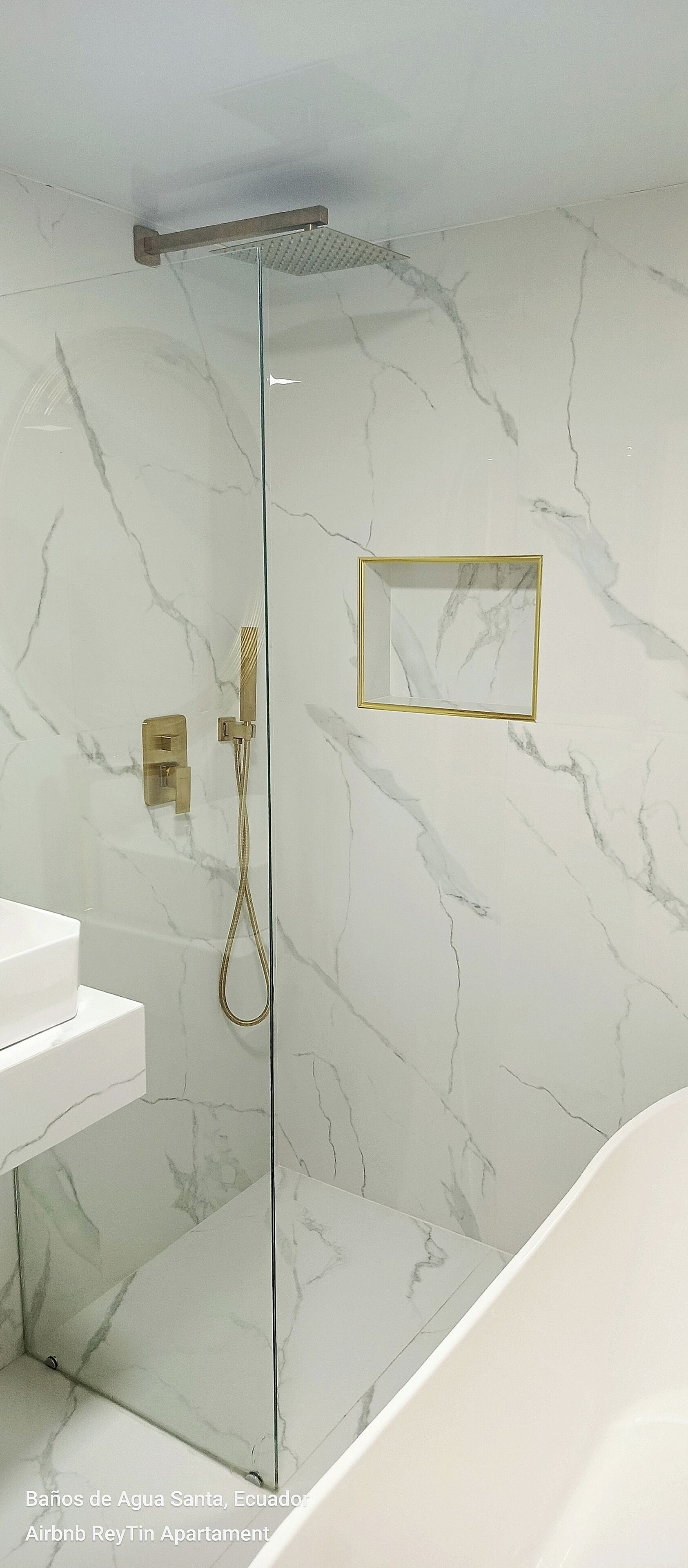 Een moderne badkamer met een douchecabine van glas, marmeren wanden en een spiegel met gouden lijst.