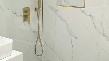 Een moderne badkamer met een douchecabine van glas, marmeren wanden en een spiegel met gouden lijst.