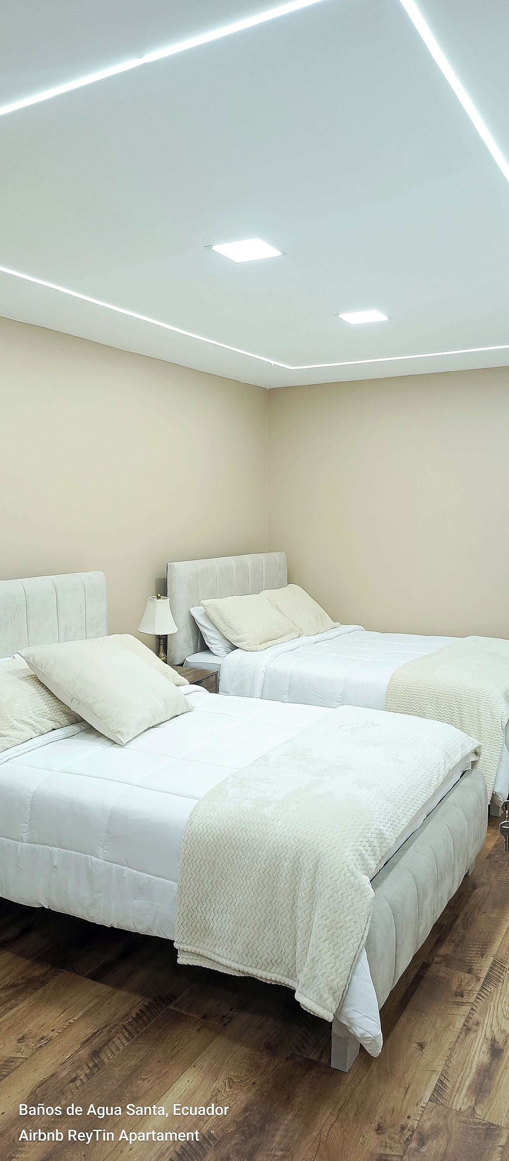 Une chambre avec deux lits, une table de chevet et un luminaire au plafond.