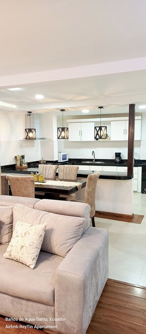 A modern kitchen with a central island, white cabinets, and a dining area with beige chairs.