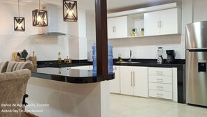 A modern kitchen with white cabinets, a stainless steel refrigerator, and a black countertop.