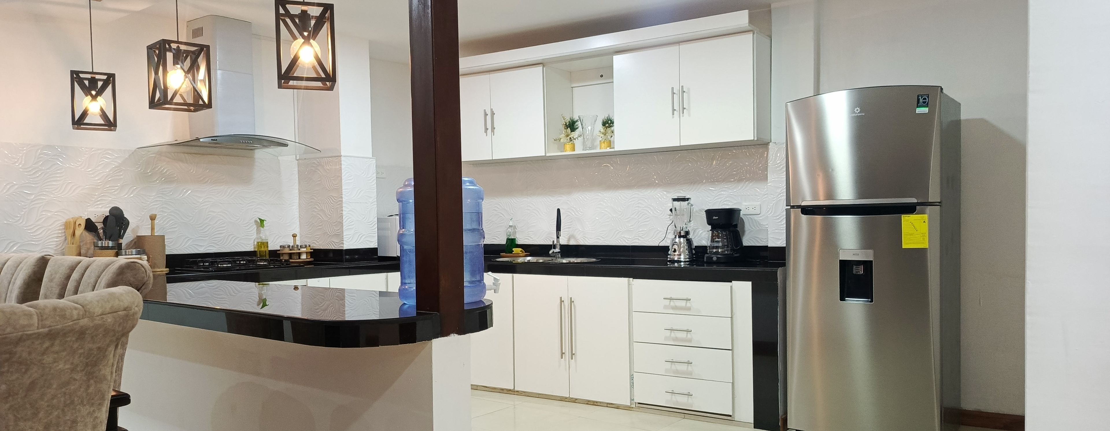 Una cocina moderna con armarios blancos, un refrigerador de acero inoxidable y una encimera negra.