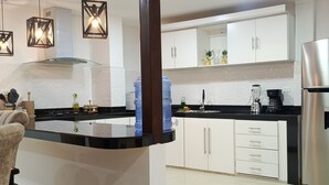 Una cocina moderna con armarios blancos, un refrigerador de acero inoxidable y una encimera negra.