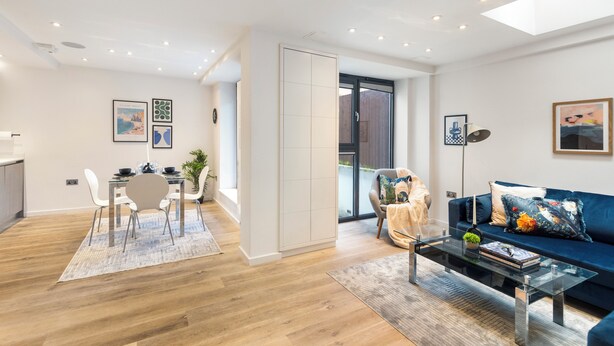 A modern living room with a glass coffee table, a blue sofa, and a dining area with a white table and chairs.