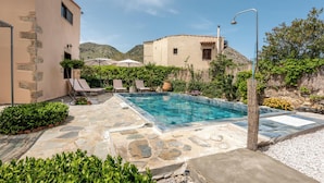 Une piscine aux bords recouverts de pierres, des chaises longues et une vue sur les montagnes en arrière-plan.