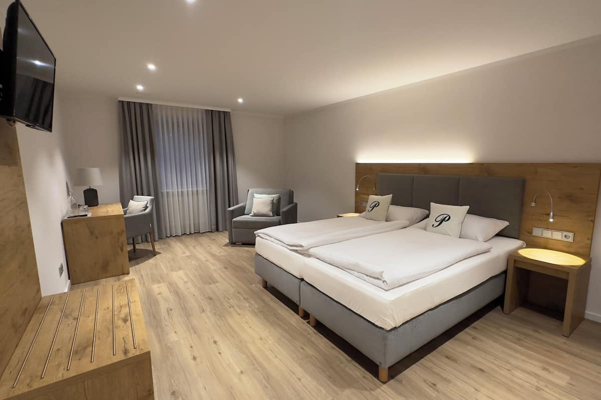 A modern hotel room with a large bed, two bedside tables, a desk, a chair, and a TV mounted on the wall.