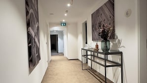 A hallway with beige carpet, white walls, and artwork. There is a reception desk with a vase and a mirror. - Hotel Gasthof zur Post Benediktbeuern (Benediktbeuern)