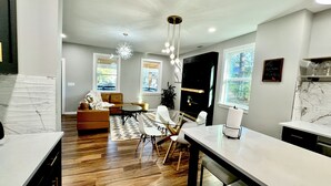 A modern kitchen with a marble countertop, a dining area with a glass table and chairs, a living room with a brown sofa, and a chandelier. - Epic Retreat at Mystic Falls-5 bd 3.5 BA-1 Mile from the Square & Clocktower (Covington)