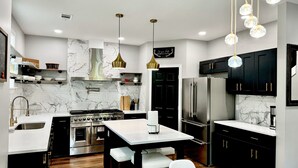 A modern kitchen with a central island, stainless steel appliances, marble backsplash, and black cabinetry. - Epic Retreat at Mystic Falls-5 bd 3.5 BA-1 Mile from the Square & Clocktower (Covington)