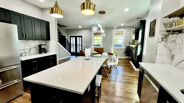 A modern kitchen with a large island, dark cabinetry, and a marble backsplash. - Epic Retreat at Mystic Falls-5 bd 3.5 BA-1 Mile from the Square & Clocktower (Covington)