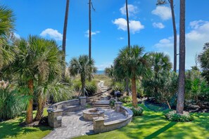 A landscaped garden with a stone fire pit, a hammock, and a pathway leading to a beach.