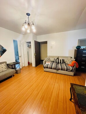 Una sala de estar con sofá, una mesa de centro y un mueble para televisión. Se ve una puerta que da a otra habitación y una escalera.