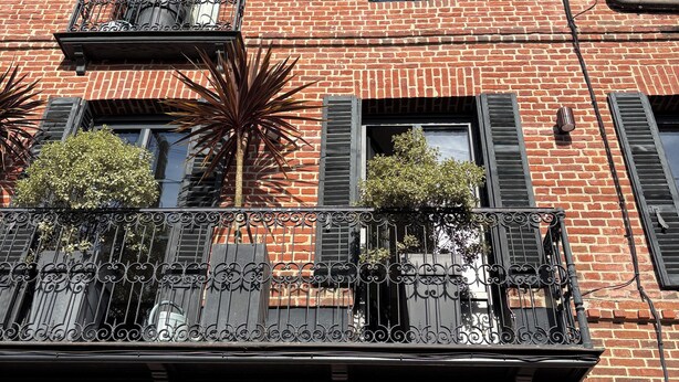A red brick building with a balcony, shutters, and a small circular window.