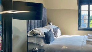 A hotel room with a bed, a desk with a laptop, a lamp, and a window.