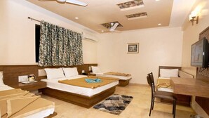 A hotel room with a large bed, a smaller bed, a desk, and a chair. There is a television on the wall and a ceiling fan. - Hotel Sai Suraj Park (Rahata)