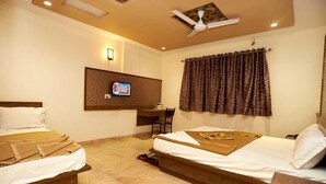 A hotel room with two beds, a desk, a ceiling fan, and a wall-mounted TV. - Hotel Sai Suraj Park (Rahata)
