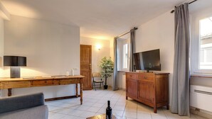 Un salon avec une table en bois, un canapé, une télévision et une bouteille de vin.