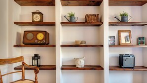 Une pièce avec des étagères en bois où sont rangés divers objets, comme une radio, un arrosoir et une lampe.