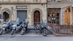 Une rangée de scooters garés et un vélo devant un immeuble où se trouve une boutique de produits gastronomiques et de vins.