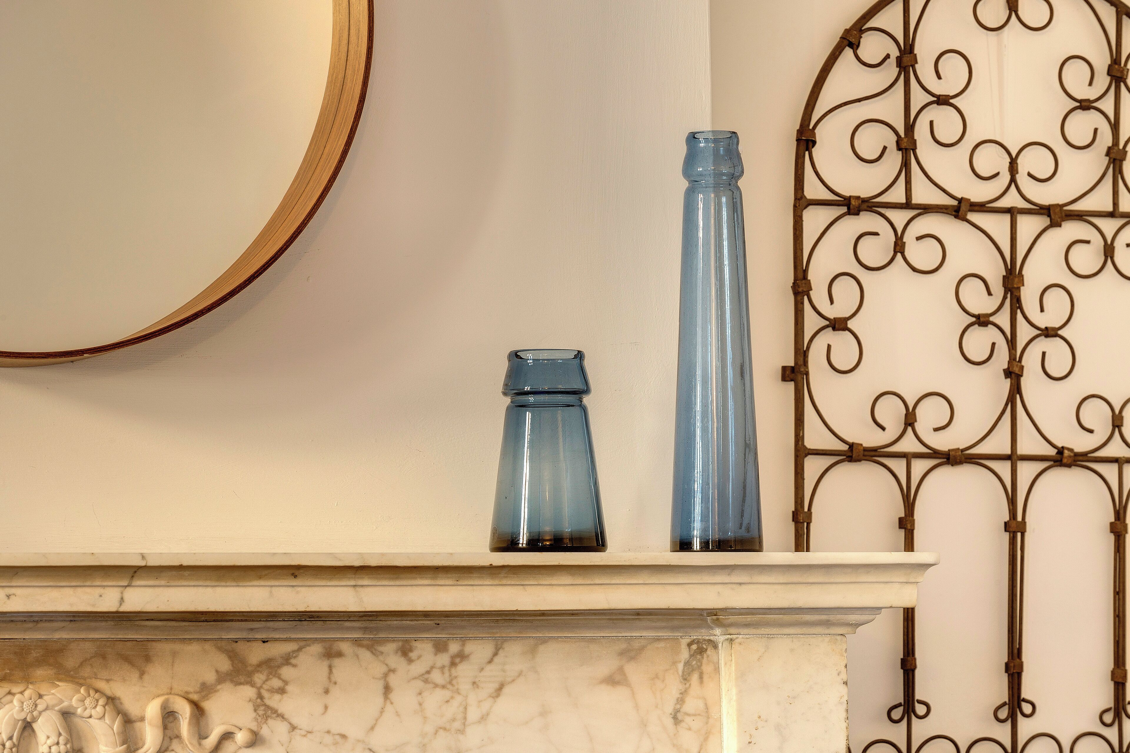 A marble fireplace mantel with two blue glass vases and a decorative metalwork piece on the wall.