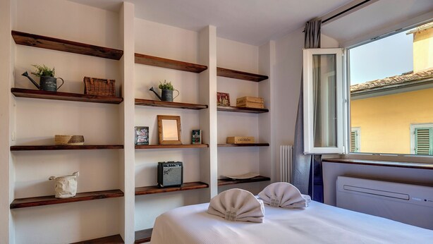 Une chambre d’hôtel avec un lit, deux oreillers, un radiateur et des étagères en bois sur lesquelles sont disposés divers objets.