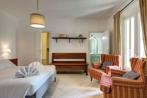 Una camera da letto con un letto, una panca, due poltrone, una pianta pensile e uno scaffale con un cesto.