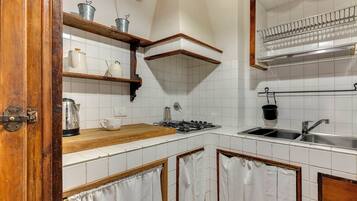 Una cocina con azulejos blancos, estantes de madera, una estufa a gas y un lavamanos.