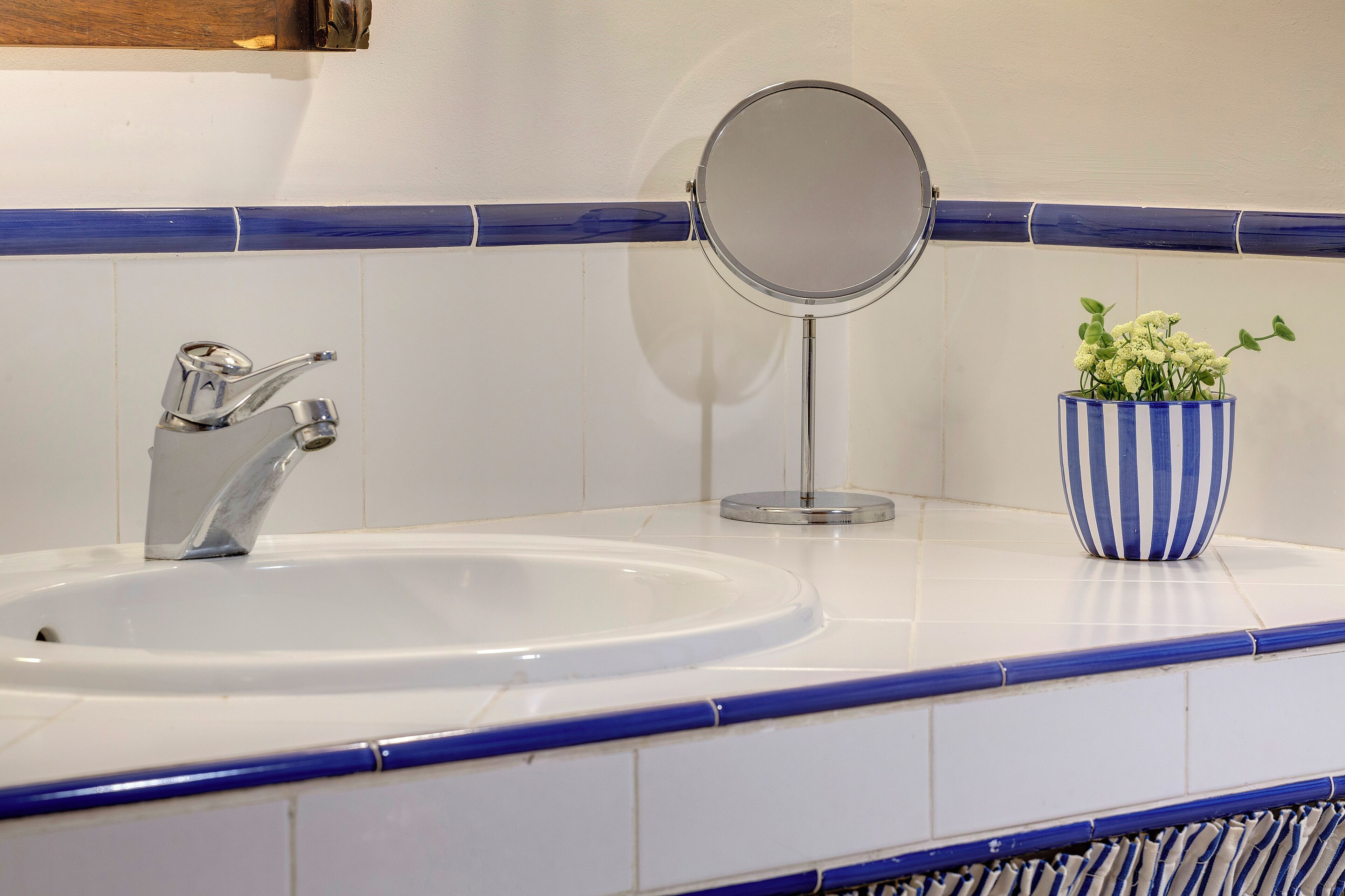 A bathroom with a white sink, a round mirror, and a striped vase with green plants.