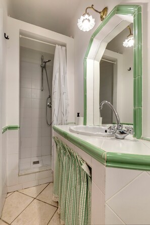 Un bagno con doccia, lavabo con specchio e asciugamani a righe verdi.