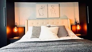 A bedroom with a bed, two bedside tables, a headboard with artwork, and wall-mounted lights. - Manchester - City Centre - Hot Tub - Free Private Parking - Sleeps 8 (Greater Manchester)