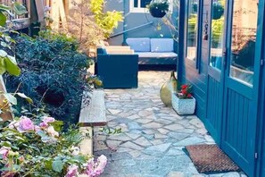 A stone-paved patio with a bench, a small table, and a potted plant. - The Dairy - Seaside Couples Escape in Whitstable (Whitstable)