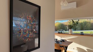Ein moderner Essbereich mit großem Fenster, einem gerahmten abstrakten Kunstwerk und einem Esstisch mit Stühlen.