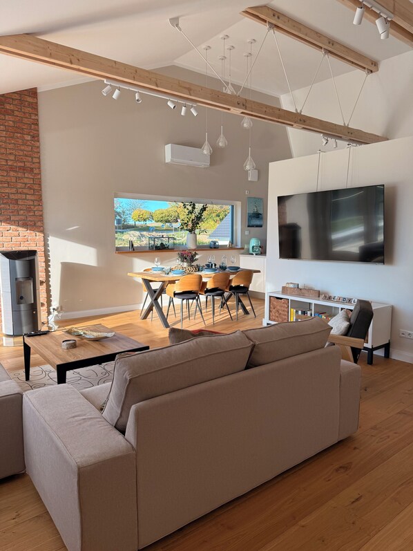Een moderne woonkamer met een bank, een eethoek met stoelen, een televisie en een open haard.