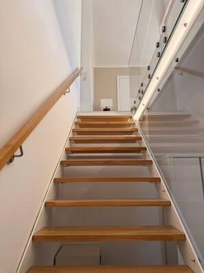 A modern staircase with wooden steps and glass railings, leading to a landing with a door and a small table. - Vacation home on Lake Möhne - designer house with plenty of space for 6 people (Möhnesee)