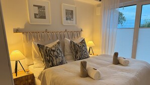 Ein helles Schlafzimmer mit einem großen Bett, zwei Nachttischen mit Lampen, einem Vorhang am Kopfteil und zwei gerahmten Bildern an der Wand.