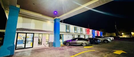 A parking lot with a motel building, cars parked, and a blue pillar.